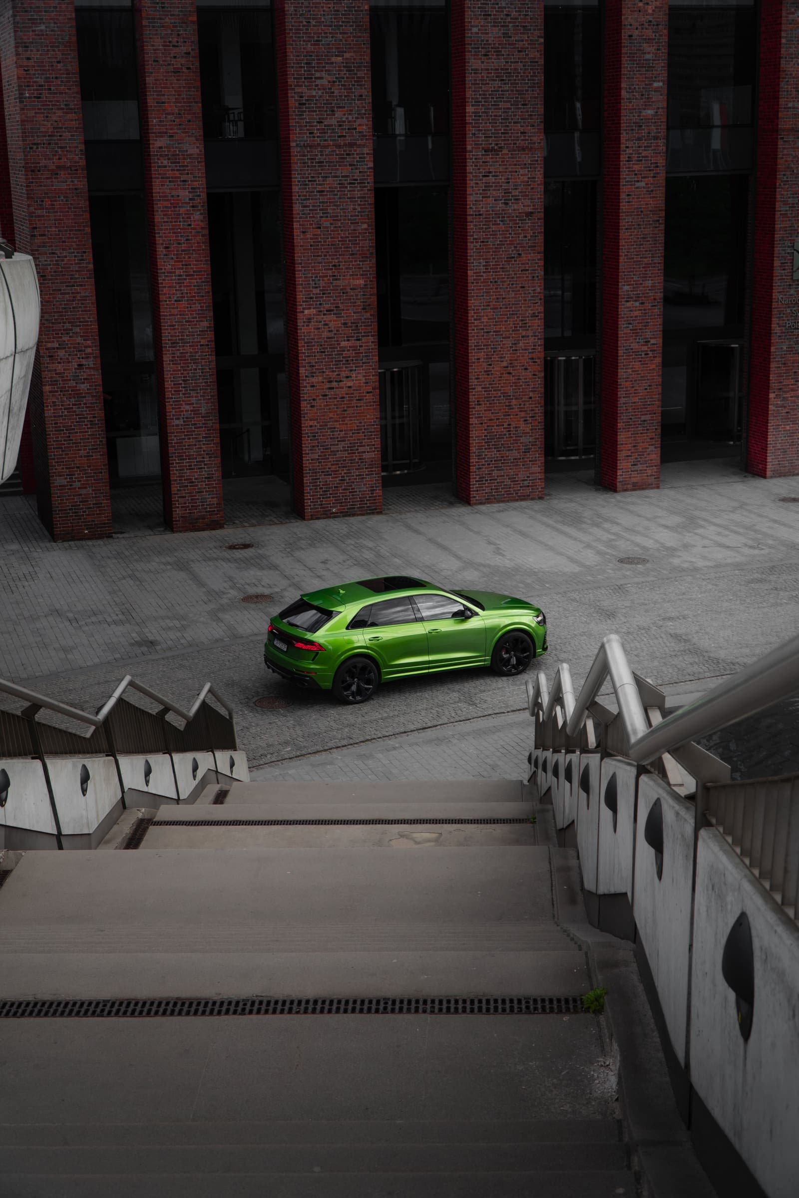 Zielone Audi RS Q8 na dziedzińcu, kadr ze schodów na tle ceglanej elewacji