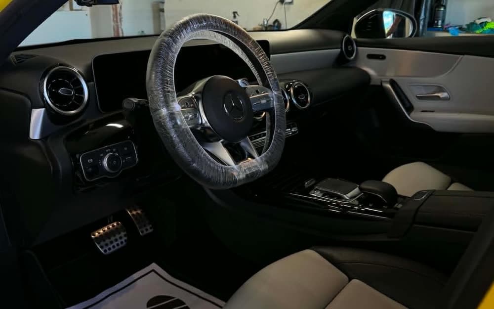 Wnętrze żółtego Mercedesa AMG w trakcie detailingu: kierownica w folii ochronnej i papierowa mata pod nogami kierowcy